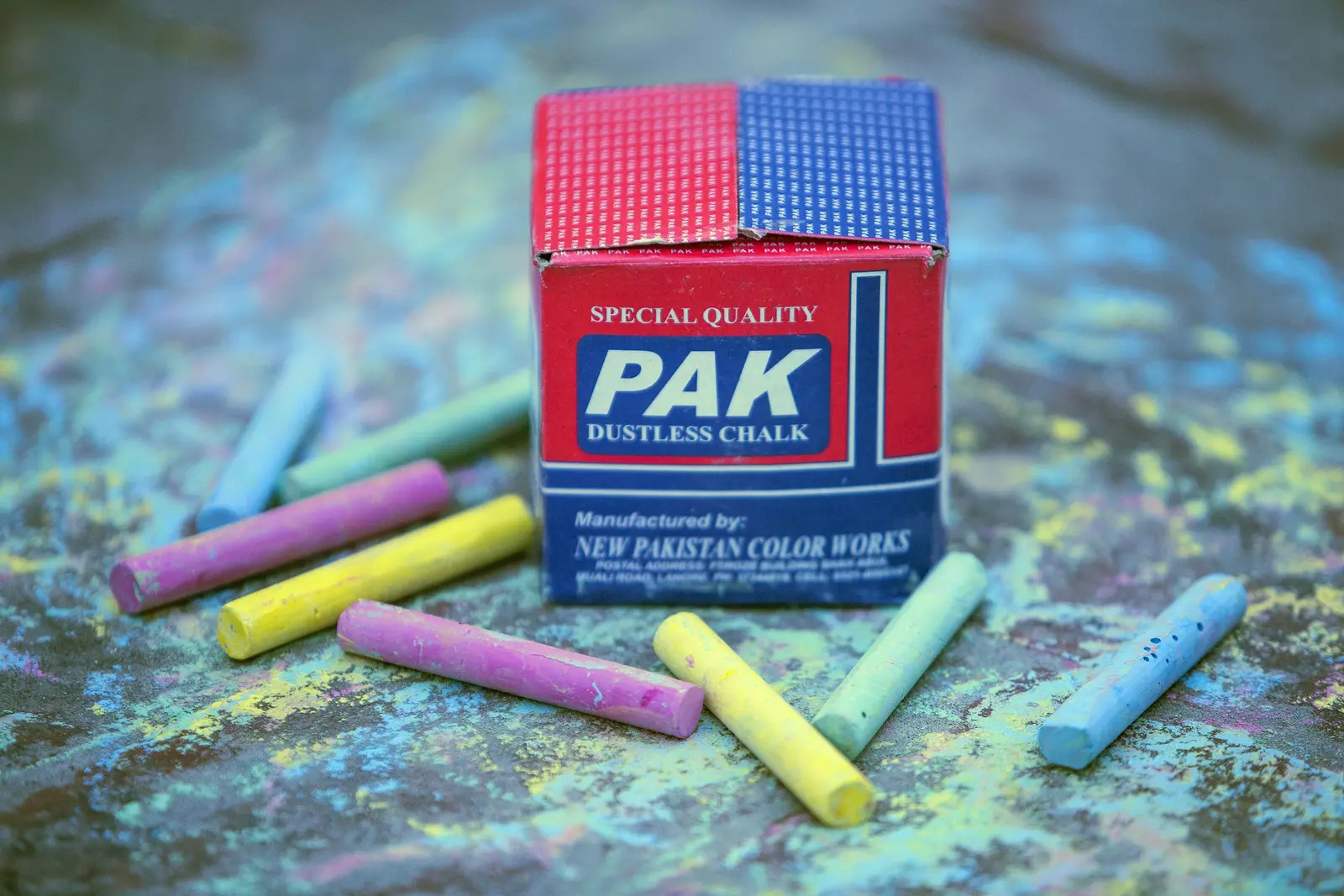 A box of PAK dustless chalk with yellow, pink, green and blue sticks around it